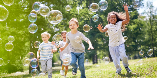 Young children chasing after bubbles and running together