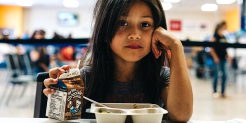 Young girl looking directly at the camera holding a fork with lunch in front